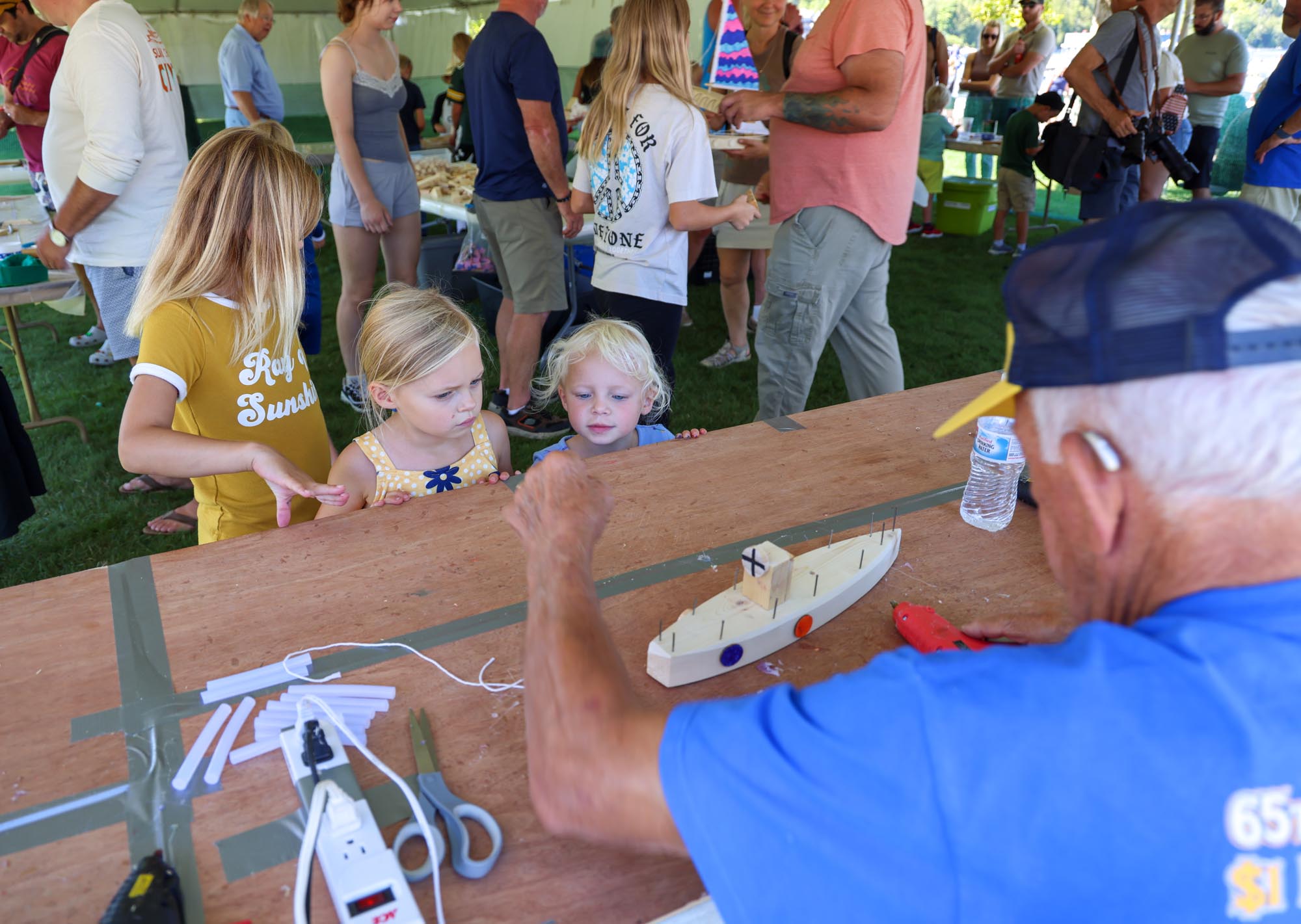 Children watching a man building a toy boat.