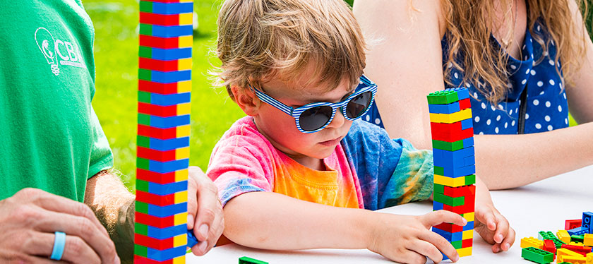 A kid with sunglasses building a tower of brick