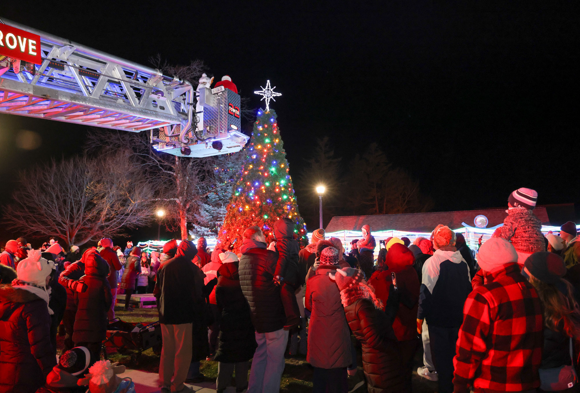 Santa lighting the christmas tree from the arm of a firetruck