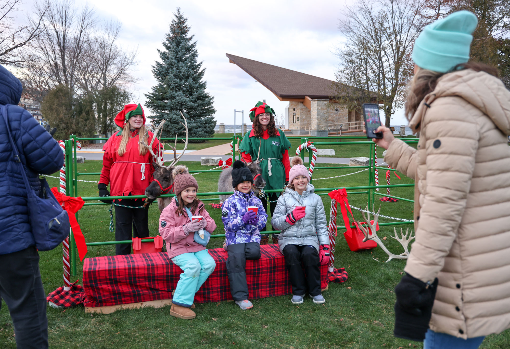 A mom taking picture of three children in front of a reindeer