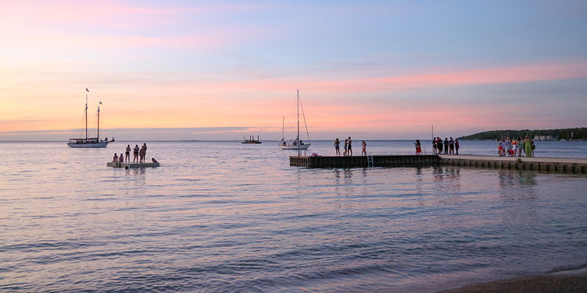 SisterBay-Website-Seasonal-Summer5-850x425_041025 Blue, orange and pink sunset over the bay with boats on the water and a pier in Sister Bay