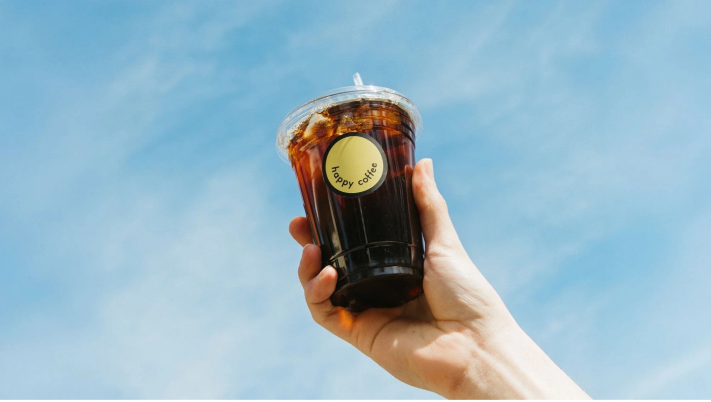 Hand holding ice coffee with happyy coffee sticker with blue sky behind it